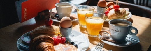 Ontbijtbord met een vegetarisch belegd broodje, croissant, pannenkoekje met vers fruit, gekookt ei, glas verse jus d'orange en een kop koffie op een sfeervol gedekte tafel